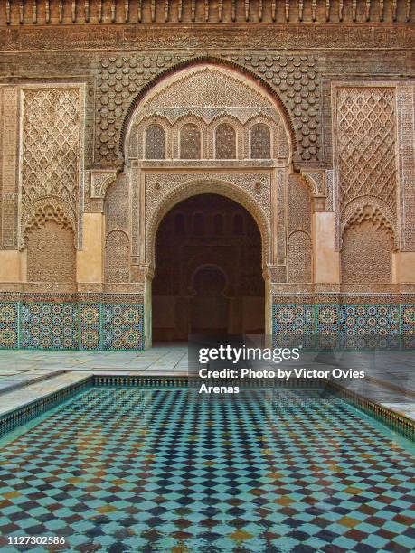 tile pond and intricate pattern of the walls and arches at the ben youssef madrasa, old islamic college in marrakesh, morocco - fountain courtyard fotografías e imágenes de stock