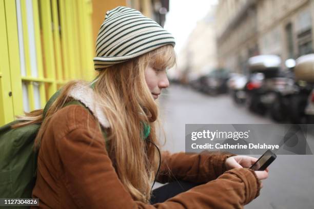 a 12 years old girl looking at his cell phone in the streets of paris - 12 13 jaar stockfoto's en -beelden