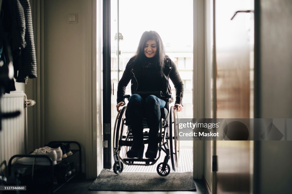 Full length of smiling young disabled woman entering home