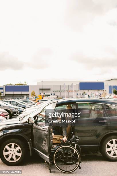 young woman sitting in car while adjusting wheelchair at parking lot against sky - open sky stockfoto's en -beelden