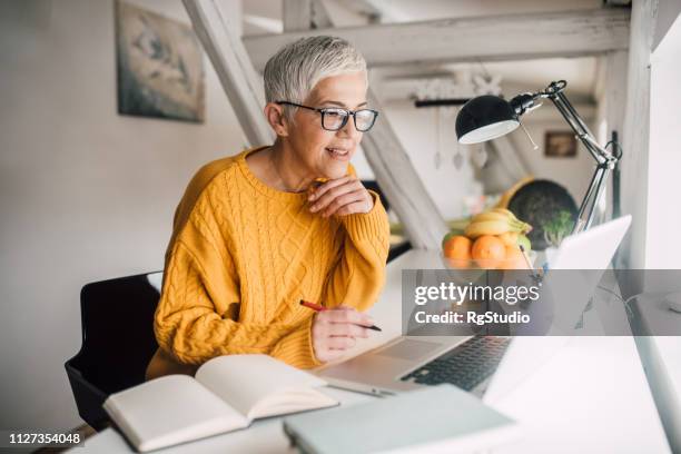 mujer mayor trabajando en ordenador portátil - educación on line fotografías e imágenes de stock