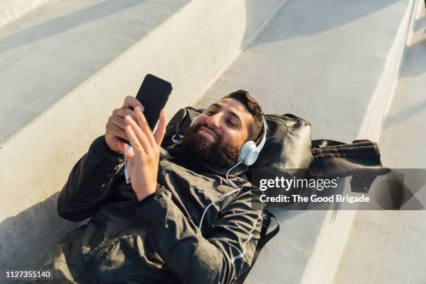 young man lying on bench in stadium listening to music on headphones - young men playing soccer stock pictures, royalty-free photos & images