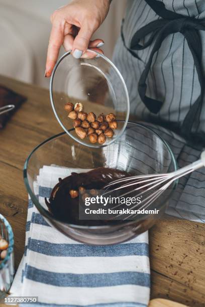 young woman mixing chocolate bowl and adding hazelnuts - chocolate pudding imagens e fotografias de stock