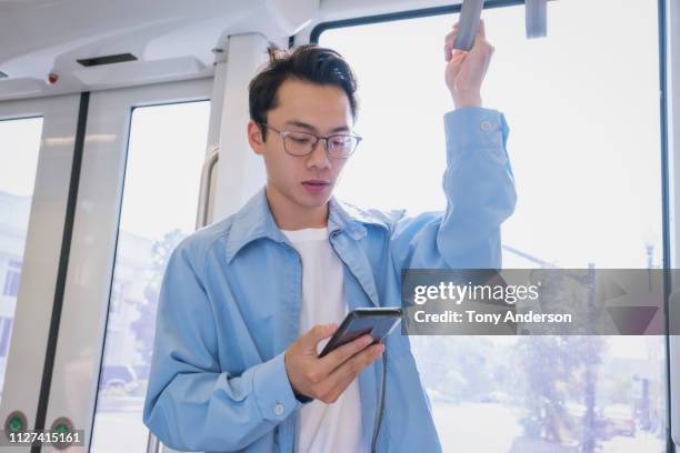 young man with mobile phone standing on commuter train - 通勤電車 ストックフォトと画像