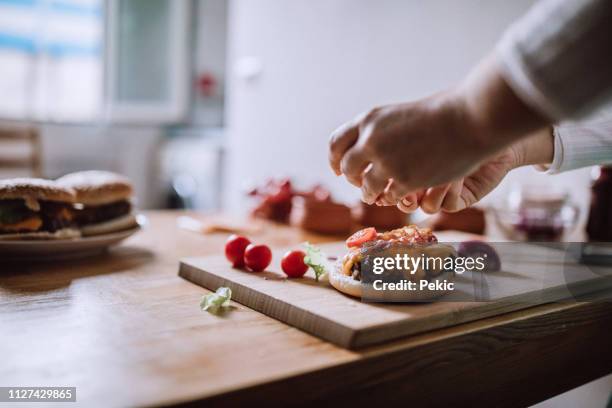 adding fresh veggies to delicious burgers - caseiro imagens e fotografias de stock