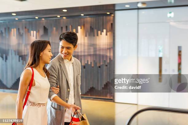 asian couple on an escalator in a shopping mall - chinese young adults shopping imagens e fotografias de stock