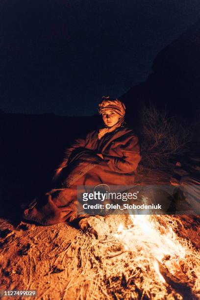nomadische frau sitzt in der nähe des feuers in der wüste wadi rum - itinerant stock-fotos und bilder