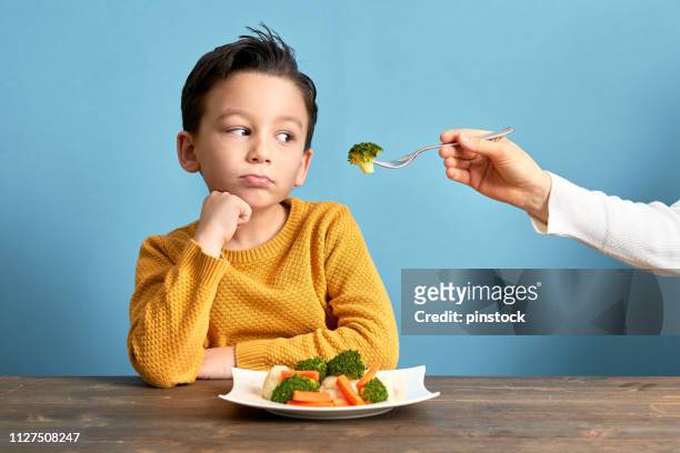child is very unhappy with having to eat vegetables. - persuasão imagens e fotografias de stock