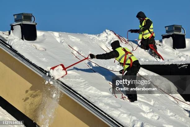 werknemers met sneeuw schoppen verrichten winter reinigen van het dak van gebouw van sneeuw en ijs - stockholm stockfoto's en -beelden