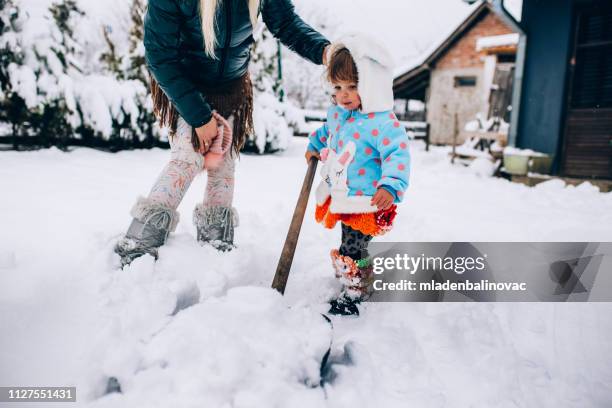 glückliche mutter genießt es, mit ihrem baby im schnee zu spielen - snow shovel stock-fotos und bilder