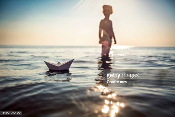 boy playing with paper boat in the sea - paper boat stock-fotos und bilder