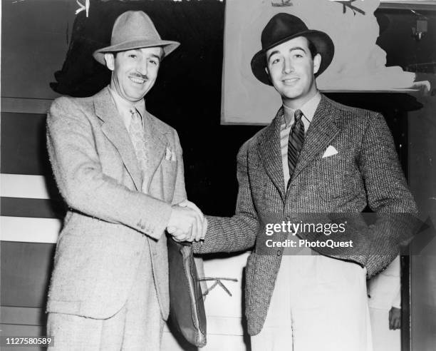 Heavily retouched portrait of American filmmaker and animator Walt Disney and actor Robert Taylor as they shake hands, 1938.