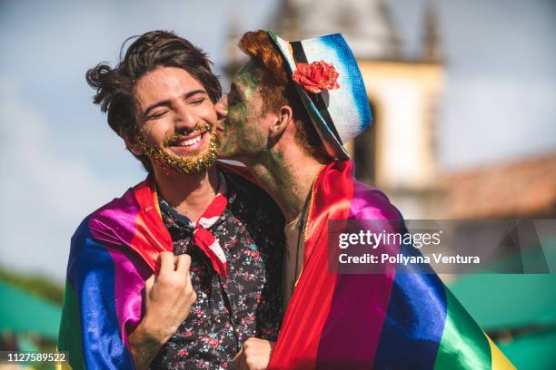 homosexual couple wrapped in rainbow flag - gay kiss stock pictures, royalty-free photos & images