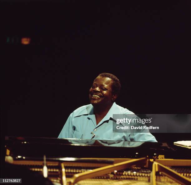 Oscar Peterson , Canadian jazz pianist, smiling as he sits behind a piano, circa 1980.