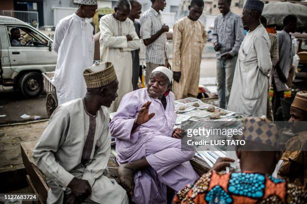 Men speaks at a newsstand with national newspapers bearing headlines announcing the victory of the incumbent President Muhammadu Buhari following...