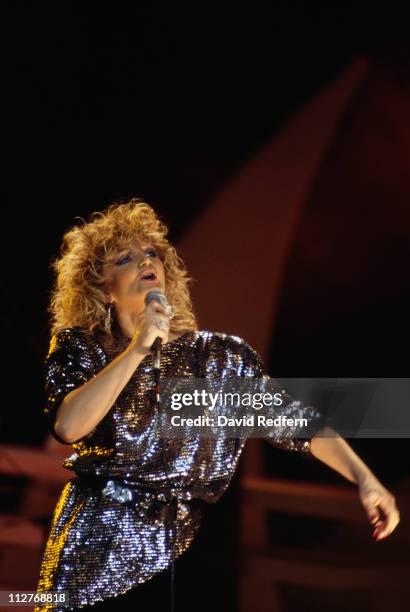 Bonnie Tyler, British singer, singing into a microphone during a live concert performance, 1986.