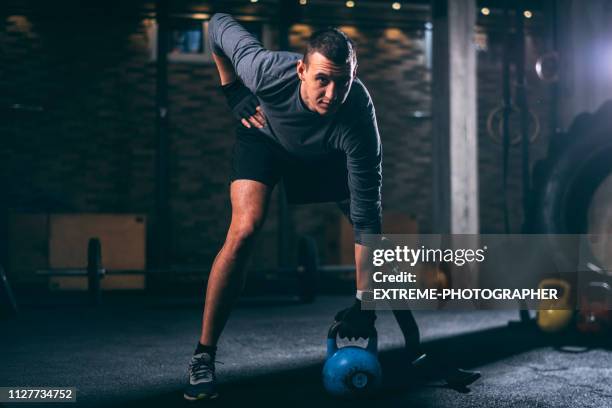 jóvenes discapacitados a atleta con una pierna protésica haciendo un una brazo kettlebell swing ejercicio en un gimnasio de forma cruzado - equipo de formación fotografías e imágenes de stock