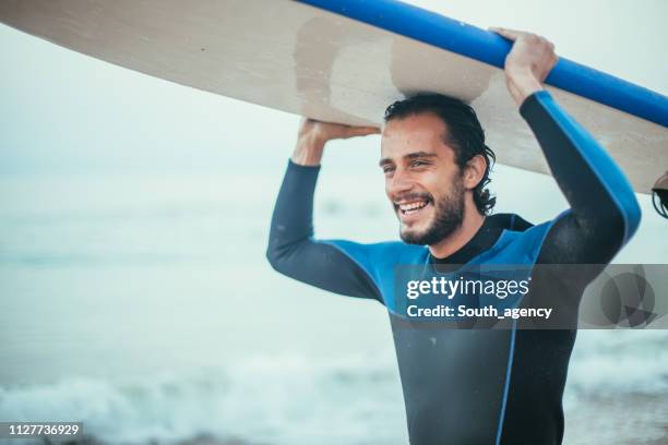 surfer carrying surfboard - wetsuit stock pictures, royalty-free photos & images