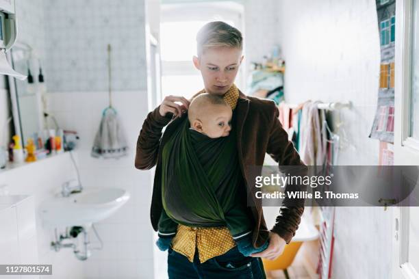 single mother putting coat on while carrying baby - androgynous boys stock pictures, royalty-free photos & images