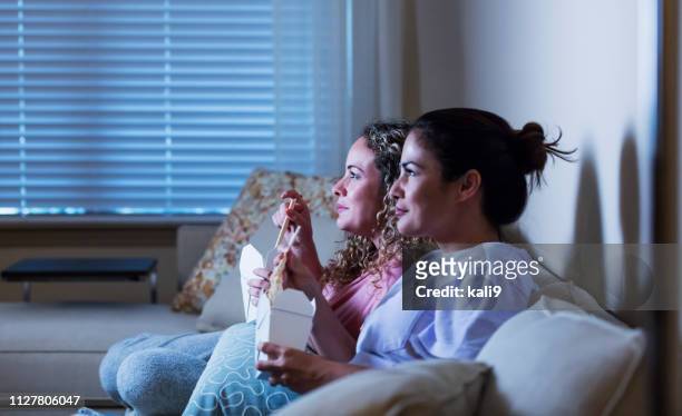 hispanic sisters on sofa eating take out, watching tv - night in stock pictures, royalty-free photos & images