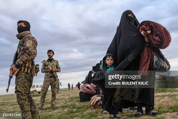 Member of the Kurdish-led Syrian Democratic Forces stand guard as a woman walks with a child after they left the Islamic State group's last holdout...