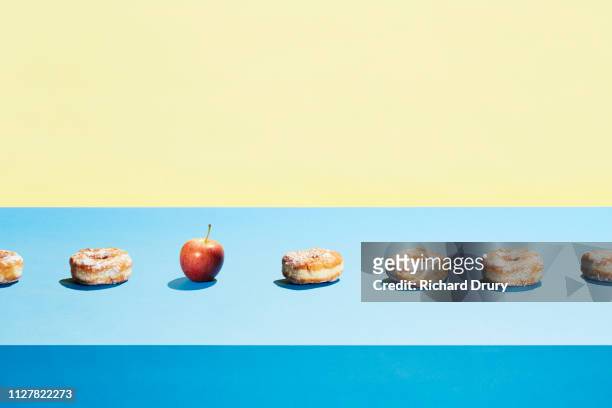 one apple in a row of donuts - temptation stock-fotos und bilder