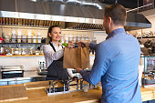 Happy waitress waring apron serving customer at counter in small family eatery restaurant. Small business and entrepreneur concept with woman owner in eatery with takeaway service delivery