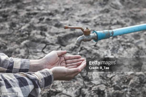 cropped image of hands catching water drop falling from faucet during drought - paisaje árido fotografías e imágenes de stock