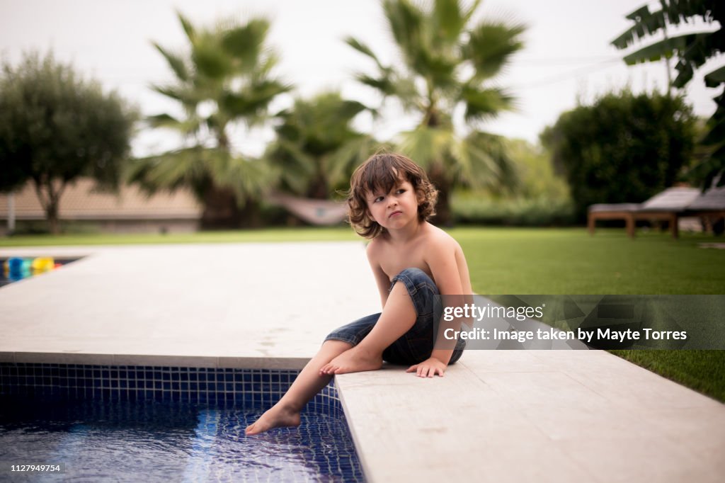 Kid sitting at the edge of the pool looking serious
