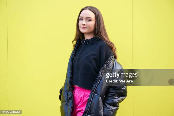 young woman in padded jacket in front of yellow background. - fossetta foto e immagini stock