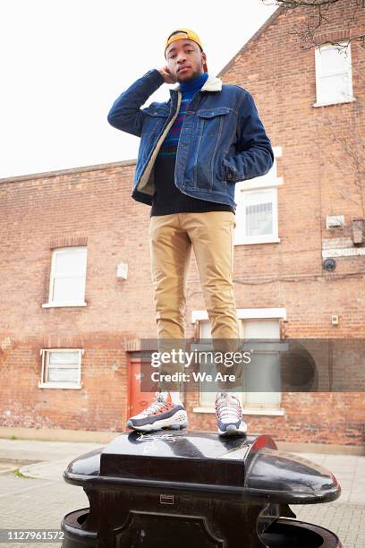 young man standing on bin in city street - khaki trousers stockfoto's en -beelden