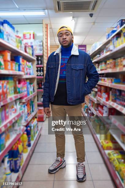 young man standing in an aisle at convenience store - corner shop stock pictures, royalty-free photos & images