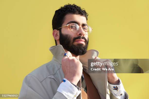 Young fashionable man holding collar of jacket.