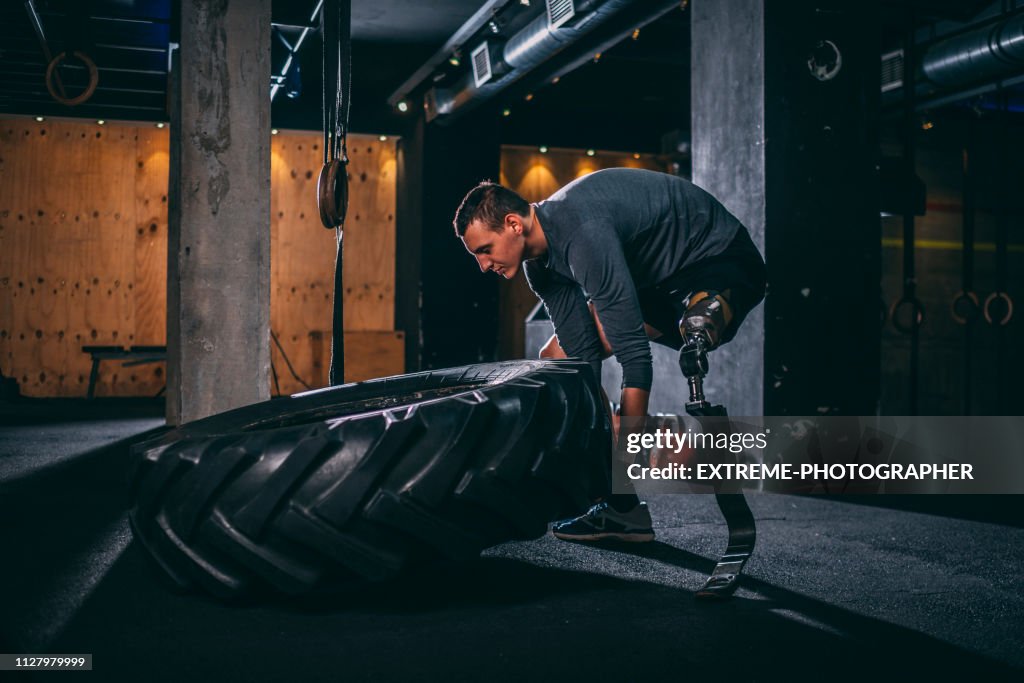 Young adaptive sportsman doing a tire flip gym exercise in a gym