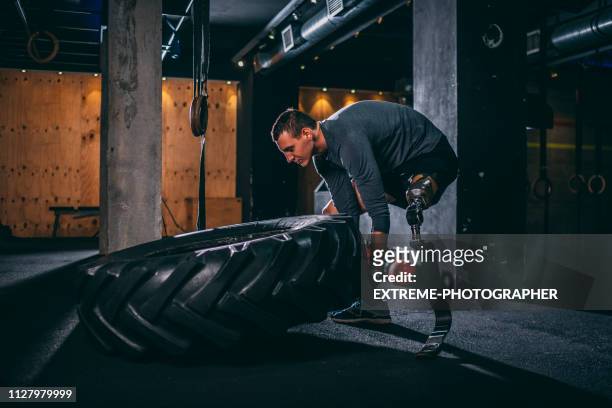 Young adaptive sportsman doing a tire flip gym exercise in a gym