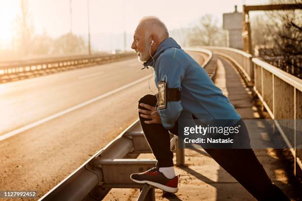 uomo anziano che si scalda per fare jogging su un ponte della città - uomini maturi foto e immagini stock