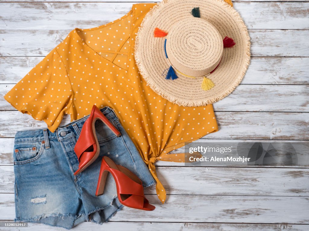 Womens vestuário, acessórios, calçados (mula couro salto sapatos, shorts jeans, blusa amarela em polka dot, palha chapéu). Roupa da moda, colecção Primavera Verão. Conceito de compras. Deita-se plana, Ver os de cima