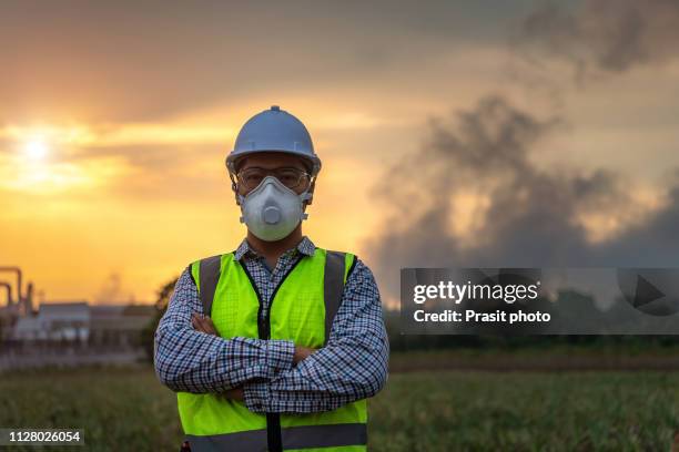 asian engineer with mask rand safety helmet in front of oil refinery and petrochemical plant with pollution - air respirator mask stock pictures, royalty-free photos & images