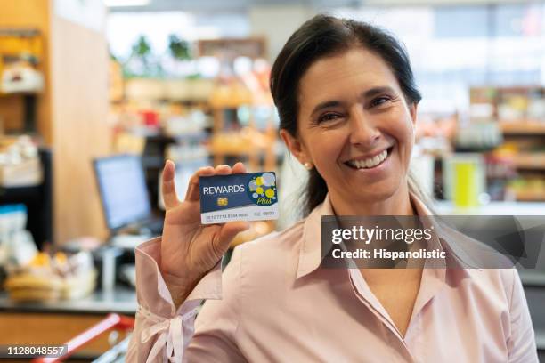 schöne weibliche erwachsene kunden im supermarkt hält eine treuekarte programm mit blick auf die kamera zu lächeln - customer loyalty stock-fotos und bilder