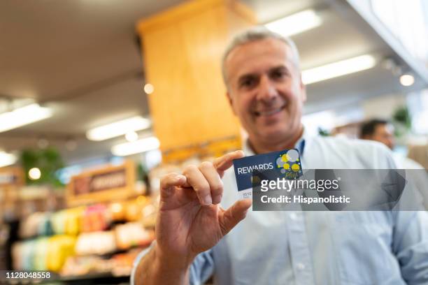 glad manliga kunden innehar ett förmånskort för program på stormarknaden inför kameran leende - loyalty card bildbanksfoton och bilder