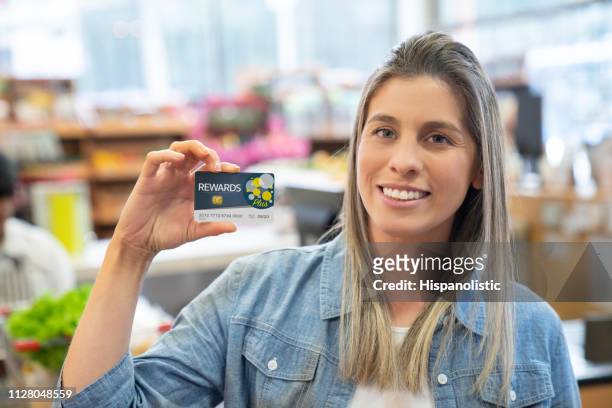 nahaufnahme eines schönen jungen kunden in einem lebensmittelgeschäft hält eine rewards karte vor die kamera zu lächeln - customer loyalty stock-fotos und bilder