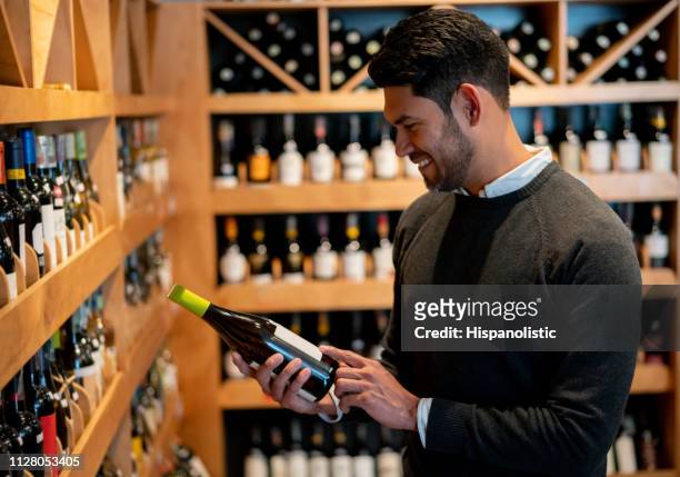 handsome man at a wine store reading the label on bottle smiling - buying alcohol stock pictures, royalty-free photos & images