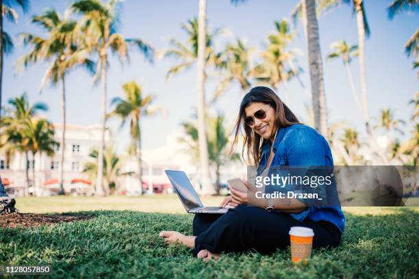 casual millennial latina using laptop in park in usa - miami business imagens e fotografias de stock