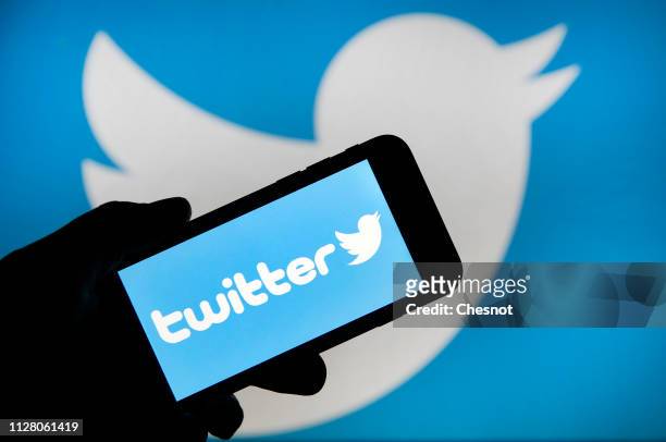 In this photo illustration the Twitter logo is displayed on the screen of an iPhone in front of a computer screen displaying a Twitter logo on...
