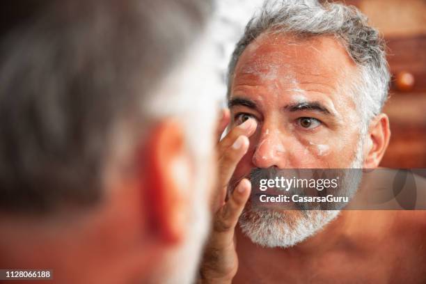 sunburned mature man moisturize his skin - rash stock pictures, royalty-free photos & images