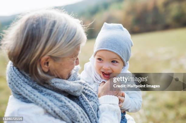 a portrait of senior grandmother outdoors holding a toddler granddaughter in nature. - mamie photos et images de collection