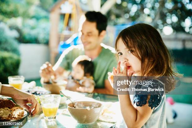 young daughter sharing breakfast with family at table in backyard - children eating breakfast stockfoto's en -beelden