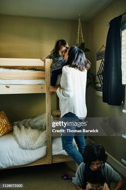 mother kissing young daughter sitting on top bunk in bedroom - litera fotografías e imágenes de stock