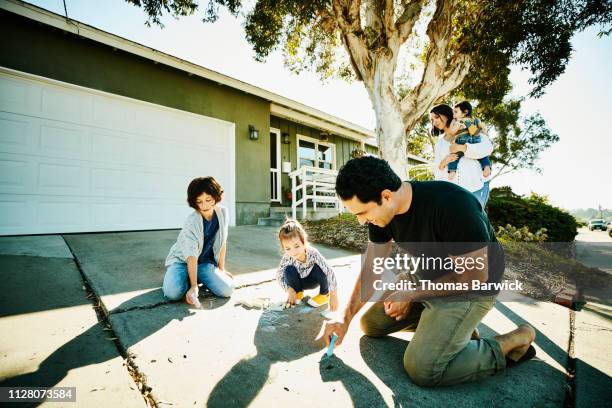 smiling father drawing chalk pictures on driveway with daughters - family chalk drawing stock pictures, royalty-free photos & images