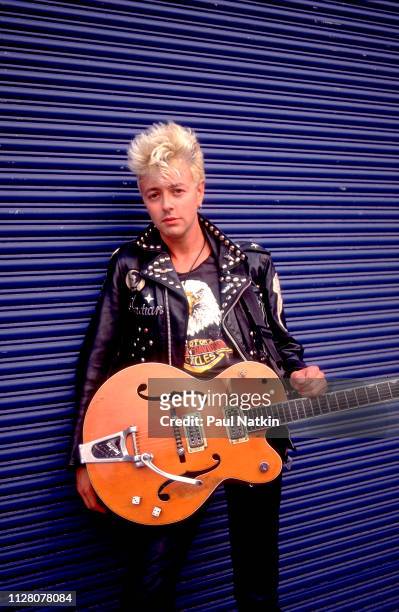 Portrait of American Rockabilly and Rock musician Brian Setzer, of the group Stray Cats, as he poses with his guitar, backstage at the Marcus...